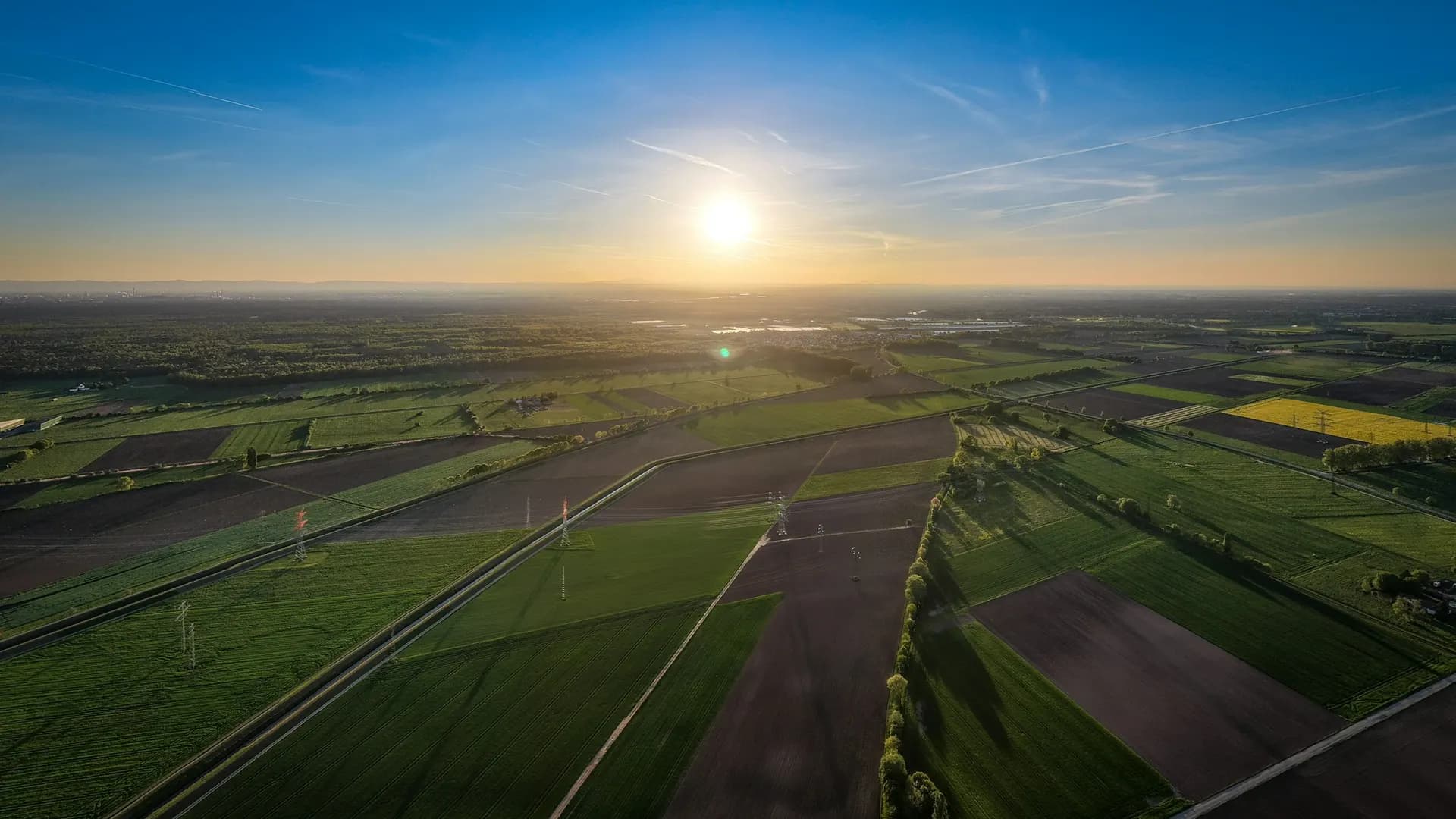 Slow aerial drift over green fields at golden hour, 15 second loop, no people, no text