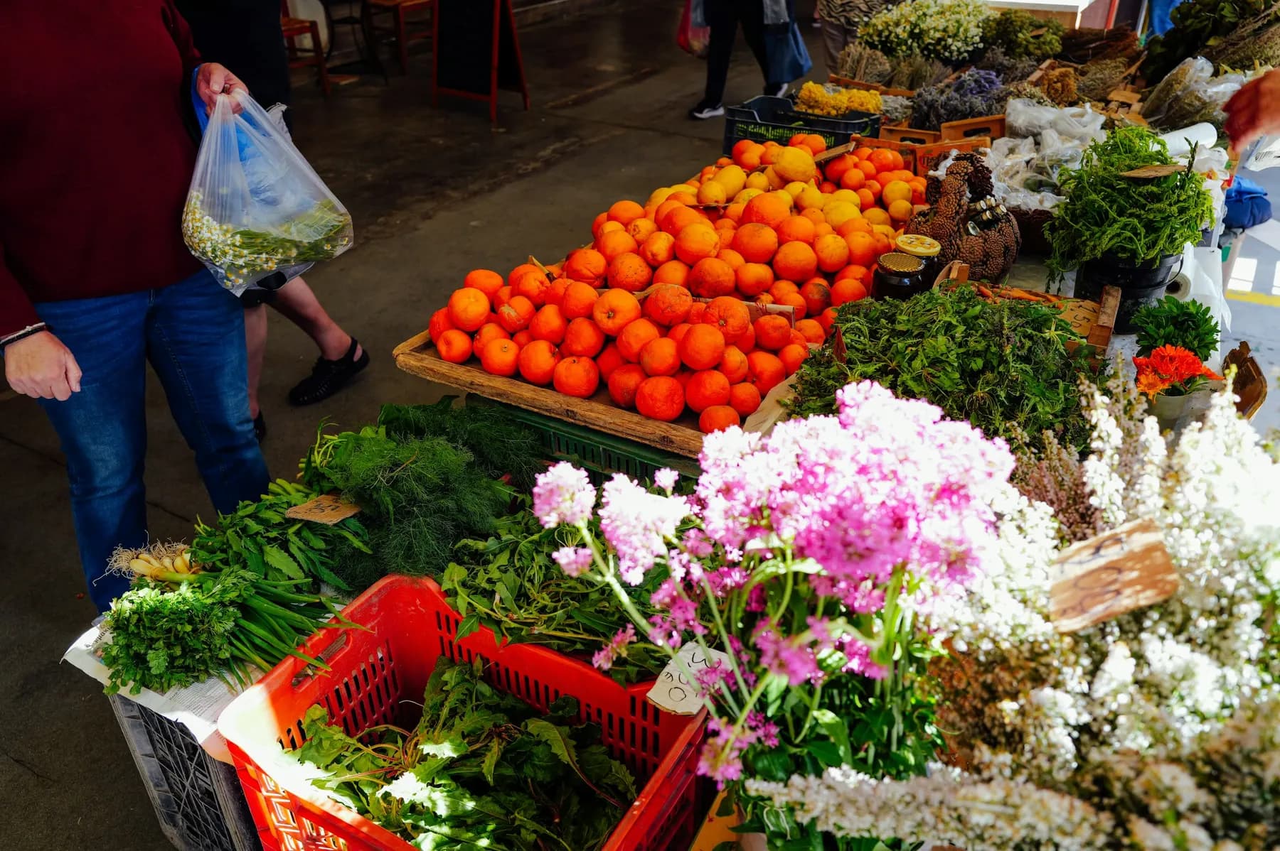 A farmers' market stall with oranges, greens and flowers